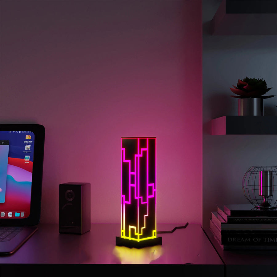 Lampe colonne en acrylique, motif labyrinthe néon allumé en rose et jaune, sur un bureau