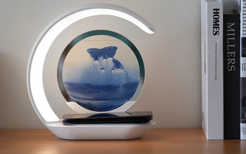 Lampe à sable animé coloris sable bleu posée sur un bureau, téléphone en charge sur le socle