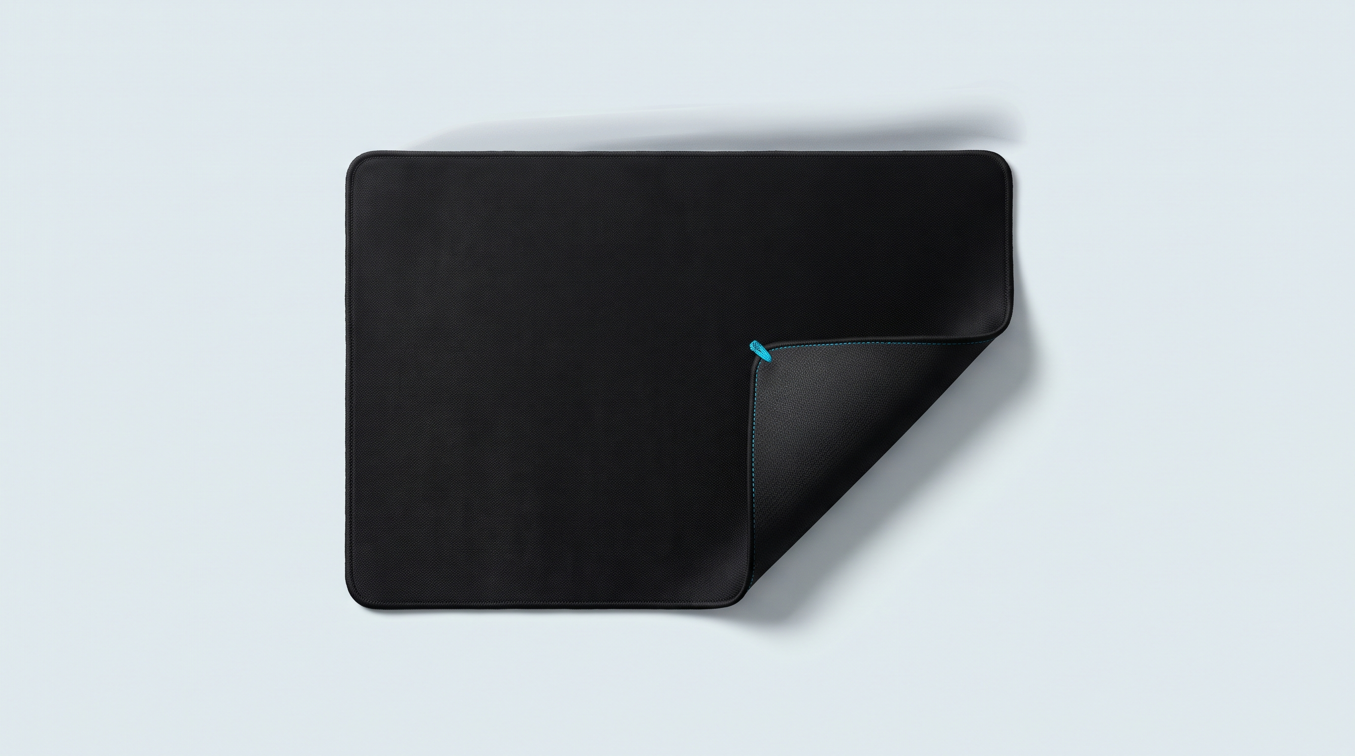 Grand tapis de bureau noir déroulé, un coin replié montrant sa surpiqûre et son dos caoutchouc