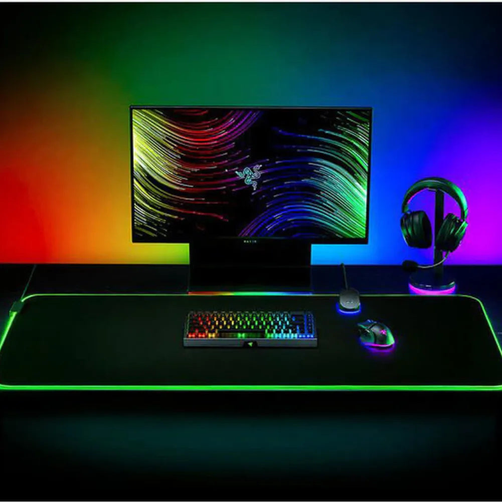 Gaming setup with Razer Goliathus Chroma 3XL RGB mouse pad, colorful monitor, keyboard, mouse, and headset.